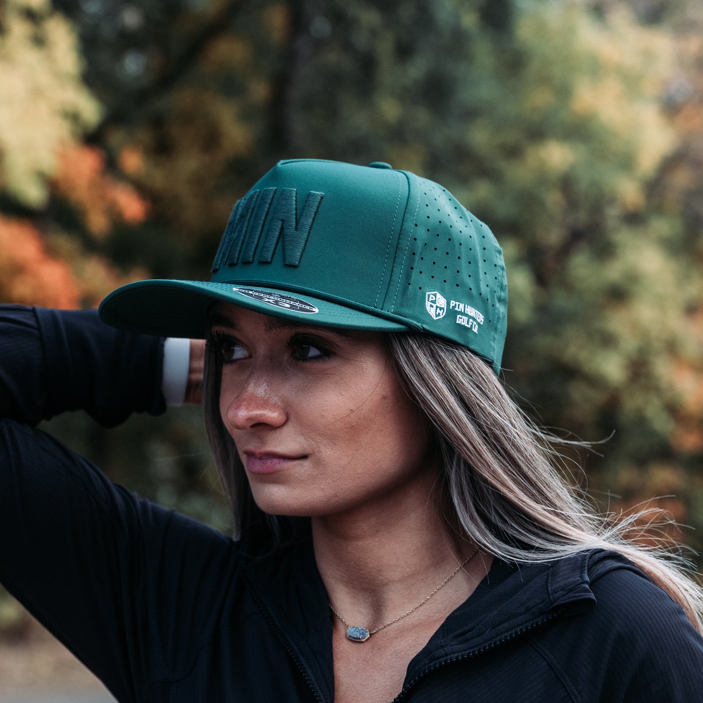 Green tonal MIN performance golf hat on model with raised matching embroidery, side logo, perforated panels, and flat brim.