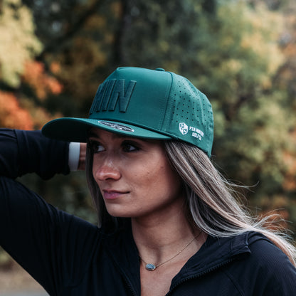 Green tonal MIN performance golf hat on model with raised matching embroidery, side logo, perforated panels, and flat brim.