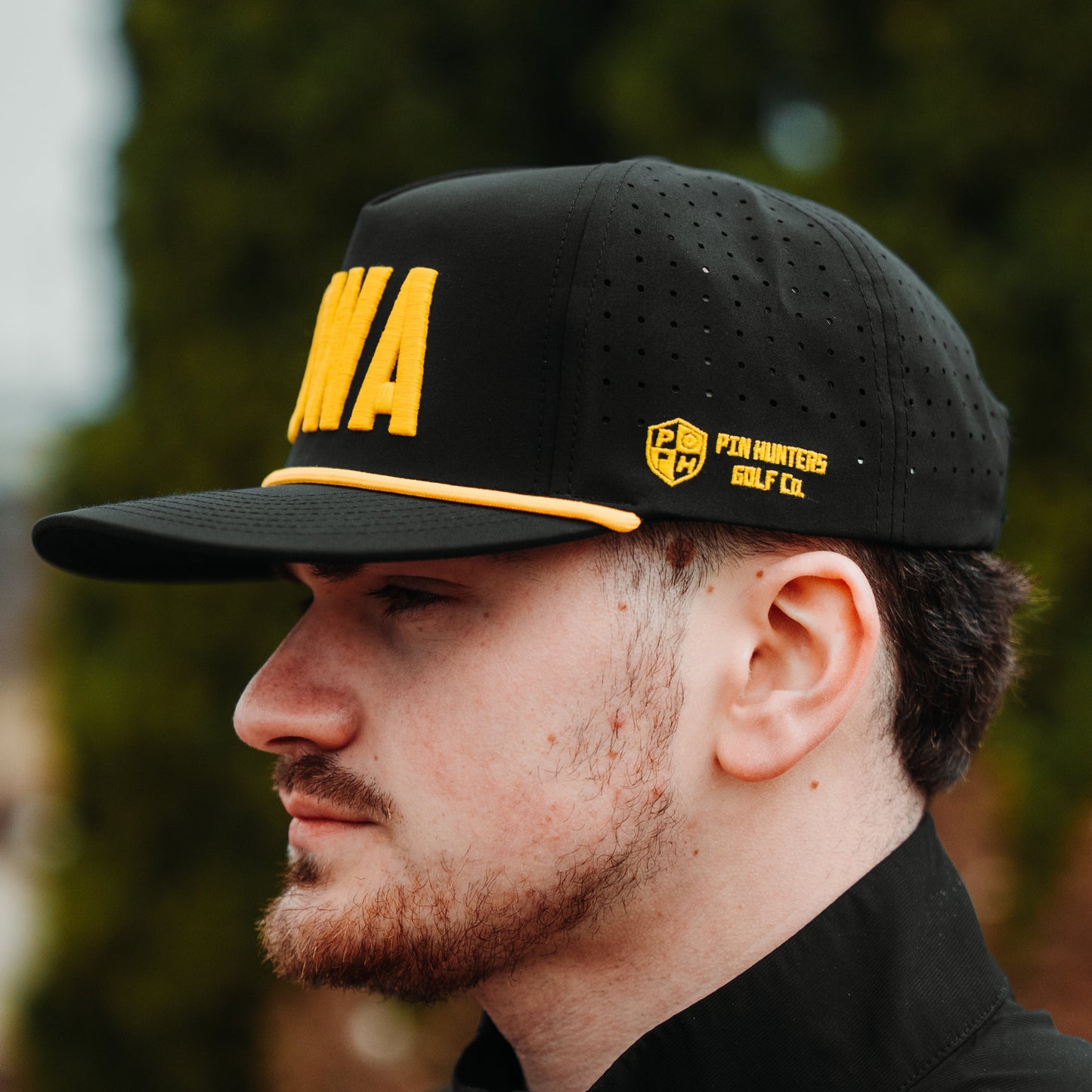 Iowa Hawkeyes inspired black IOWA performance hat with gold embroidery, gold rope detail, perforated side panels, and side logo embroidery.