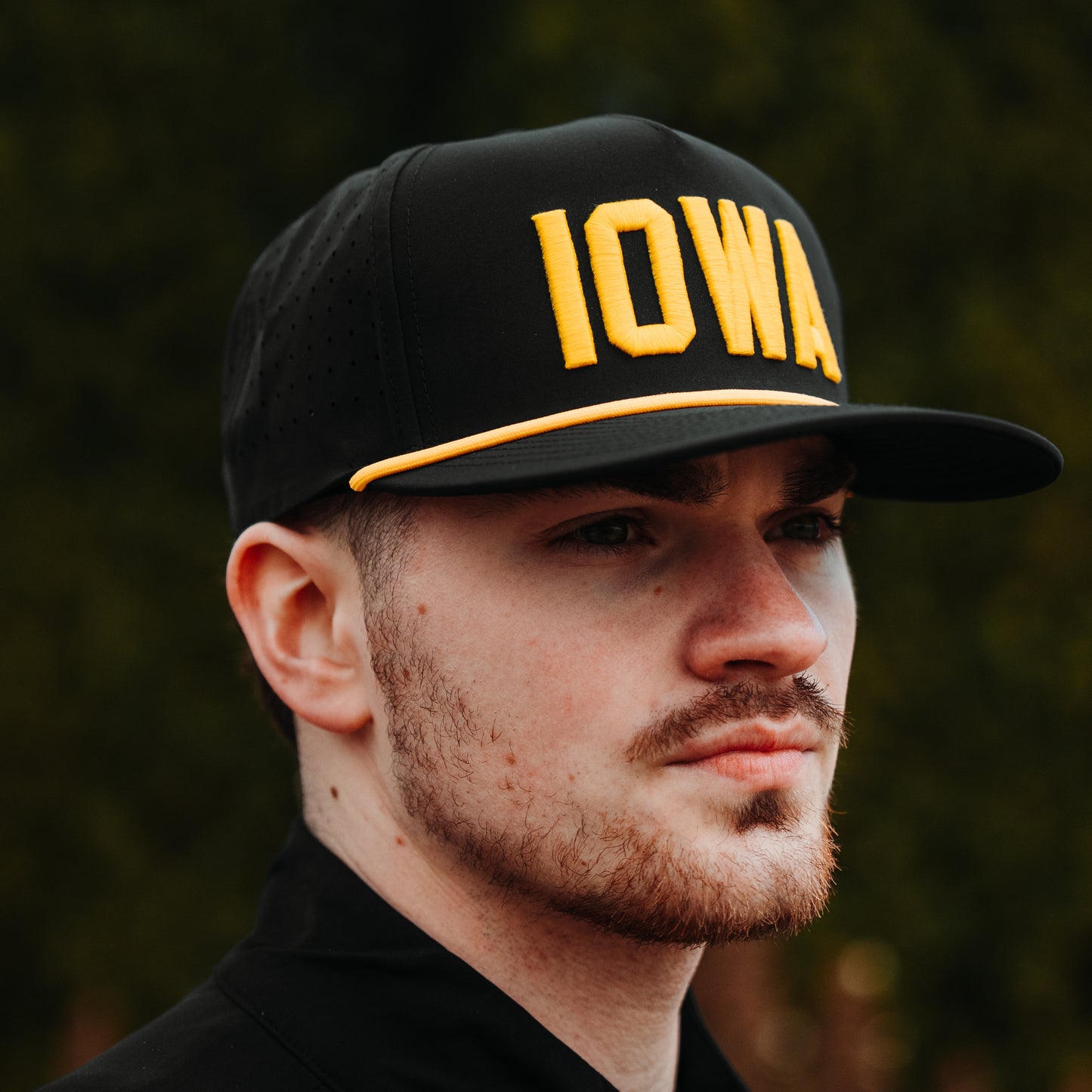Iowa Hawkeyes black performance hat lifestyle angle with yellow IOWA raised embroidery, yellow rope detail, black brim, and perforated side panels.