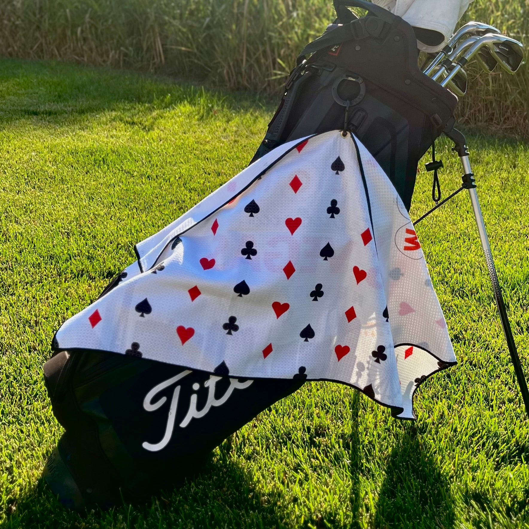 Las Vegas golf towel hanging from a black golf bag, showing the playing card suit back pattern with hearts, diamonds, clubs, and spades.