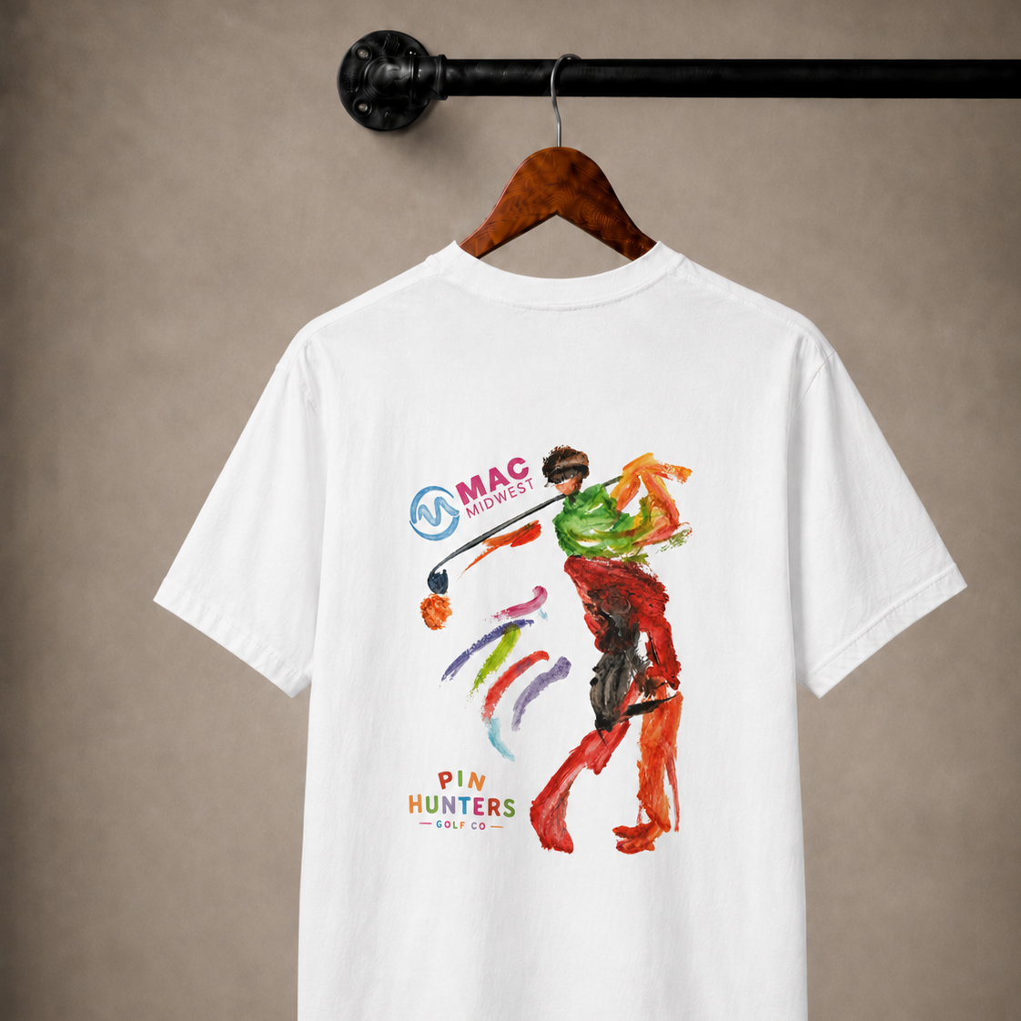 White MAC tee hanging from a wooden hanger with MAC Midwest and colorful golfer artwork on the back.