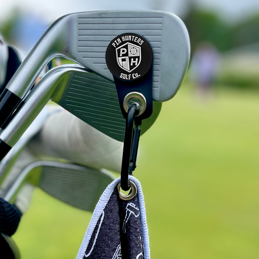 Pin Hunters Mag Towel adapter clipped to a golf club face and attached to a golf towel, showing the removable magnetic towel attachment in use.