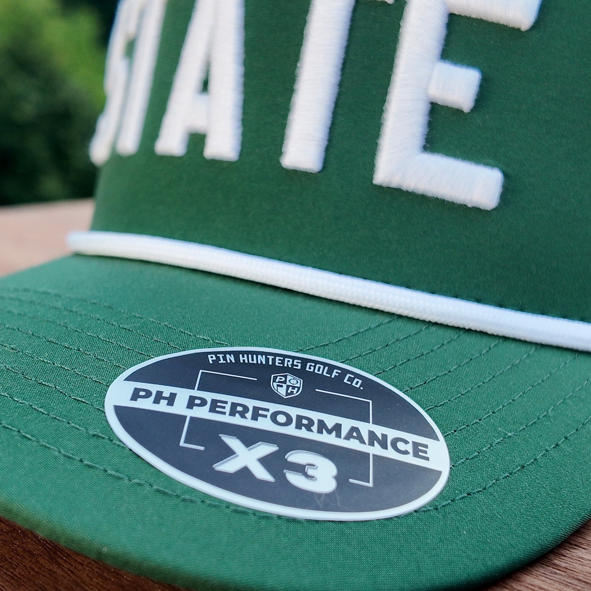 Close up of the Michigan State performance golf hat showing green brim, white rope, raised white STATE embroidery, and PH Performance X3 sticker.