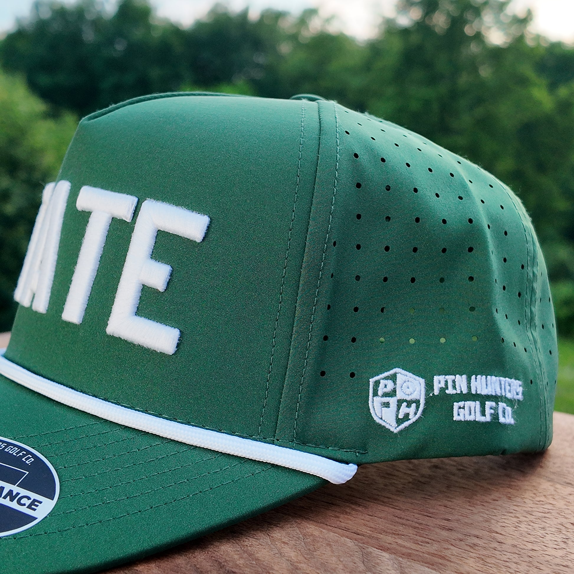 Close up side detail of the Michigan State green performance golf hat with white STATE embroidery, perforated side panel, white rope, and Pin Hunters side logo.