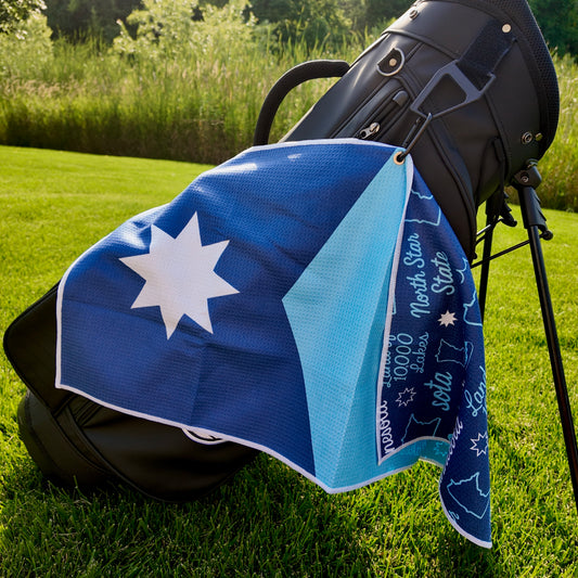 Minnesota flag golf towel hanging on a black golf bag with blue, light blue, and white Minnesota flag front design and matching Minnesota themed back pattern.