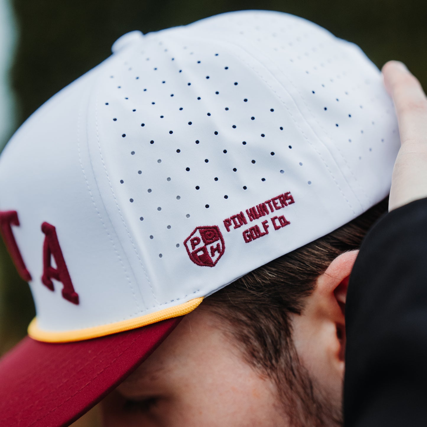Minnesota Golden Gophers SOTA hat side detail with white perforated panels, maroon PH embroidery, yellow rope, and red brim.