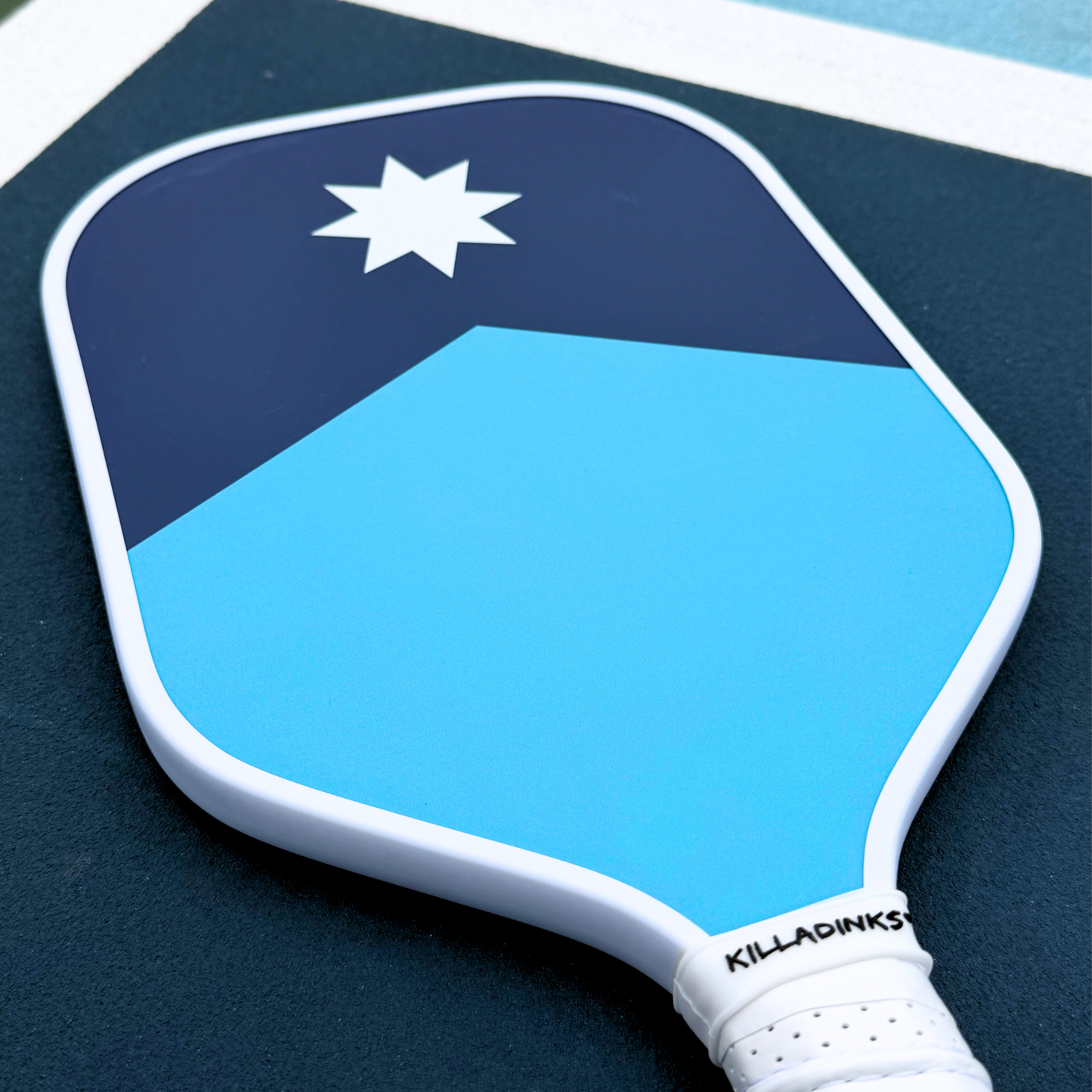 Blue North Star pickleball paddle close-up with navy upper section, light blue lower section, white star, and white edge.