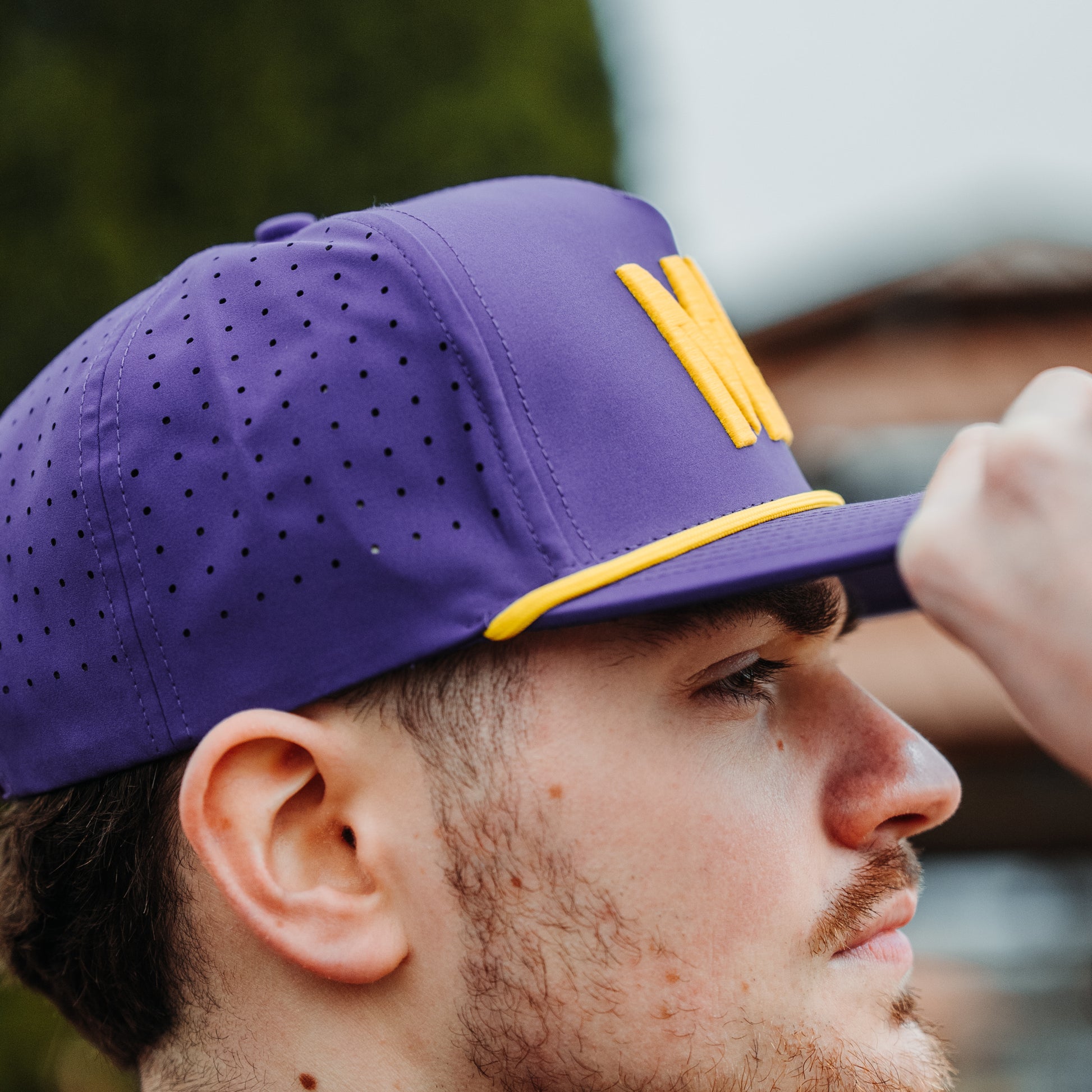 Minnesota Vikings inspired purple MIN performance hat with yellow embroidery, yellow rope detail, perforated side panels, and model side view.
