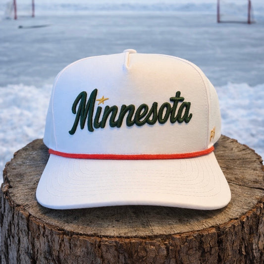 Minnesota Wild inspired white performance hat with green script embroidery, gold star accent, red rope detail, and snowy outdoor stump background.