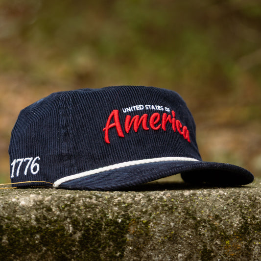 Navy corduroy America rope hat with red United States of America embroidery, white rope detail, curved brim, and 1776 side embroidery.