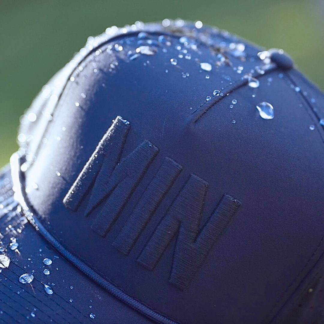 Navy tonal MIN performance golf hat close-up with matching raised embroidery, water droplets, and navy performance fabric.