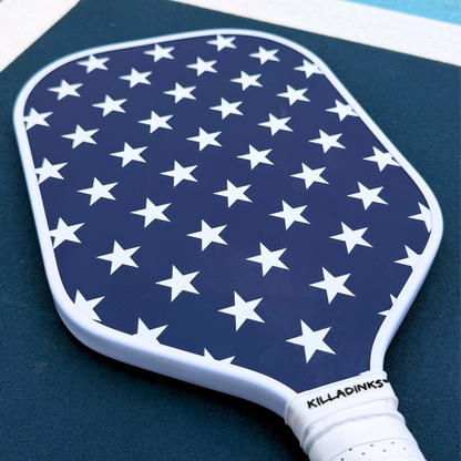 Navy pickleball paddle close-up with white stars, white edge guard, white grip, and Killa Dinks branding.