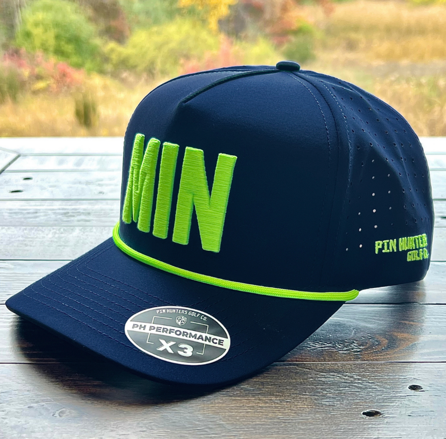 Navy MIN performance golf hat with neon lime raised embroidery, matching rope, perforated side panels, and Pin Hunters side logo.