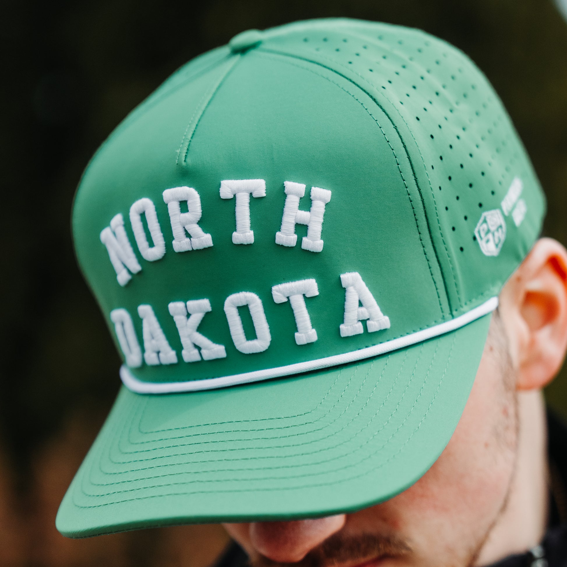 Green North Dakota performance hat with white raised embroidery, white rope detail, perforated side panels, and side logo embroidery.