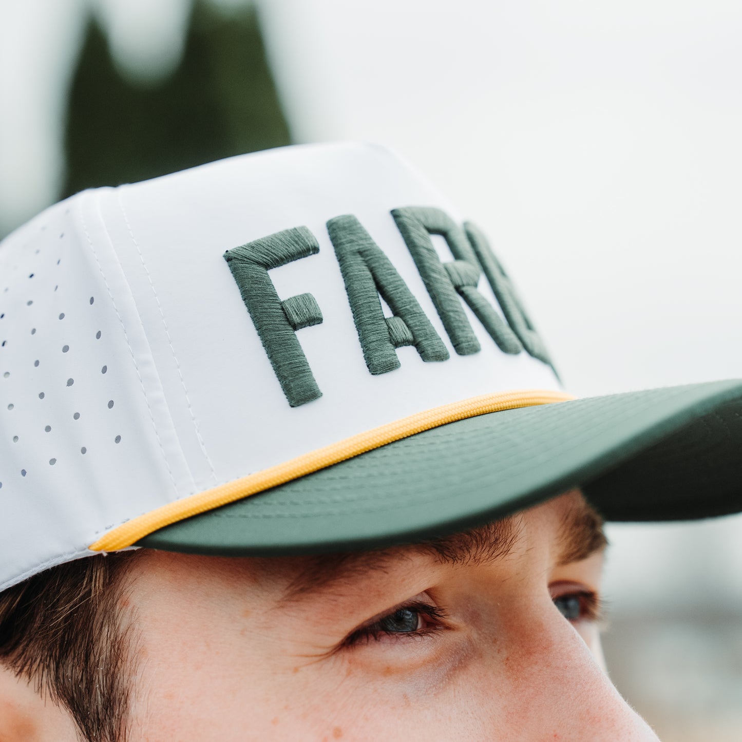 North Dakota State Bison Fargo performance hat close-up with white crown, green raised embroidery, green brim, yellow rope, and perforated side panels.
