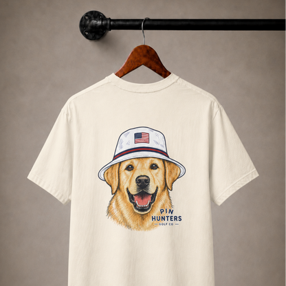 Beige/tan Pin Hunters Colby Tee displayed on a wooden hanger with golden retriever golf graphic and Pin Hunters logo on the back.