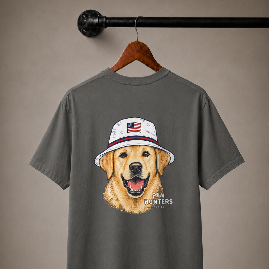 Pepper gray Pin Hunters Colby Tee on a wooden hanger with golden retriever bucket hat artwork and Pin Hunters Golf Co. logo.