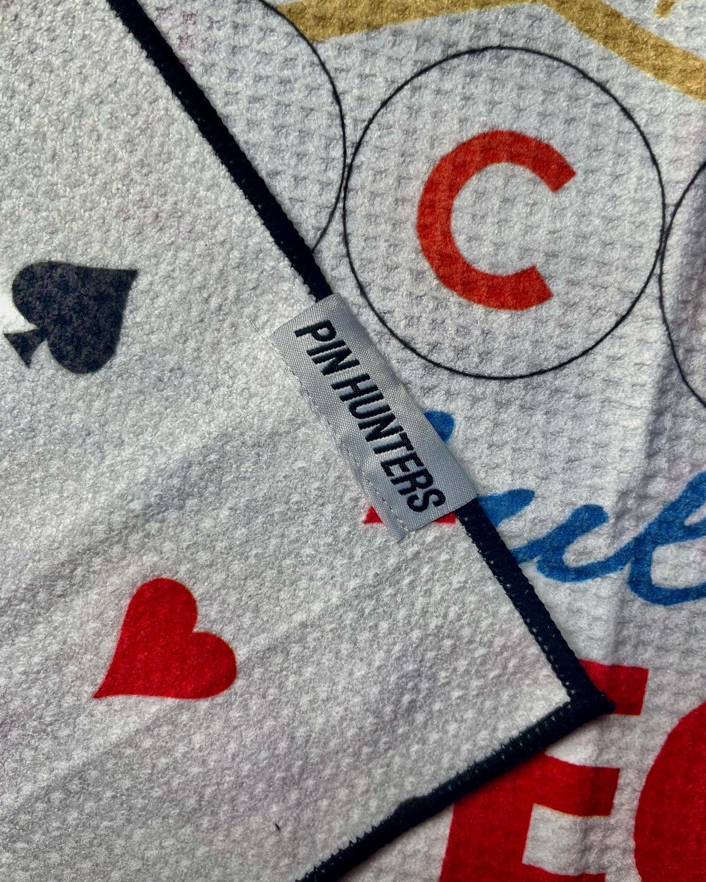 Close up of a Pin Hunters label on a Chicago Cubs inspired golf towel with red, blue, black, and gold printed details.