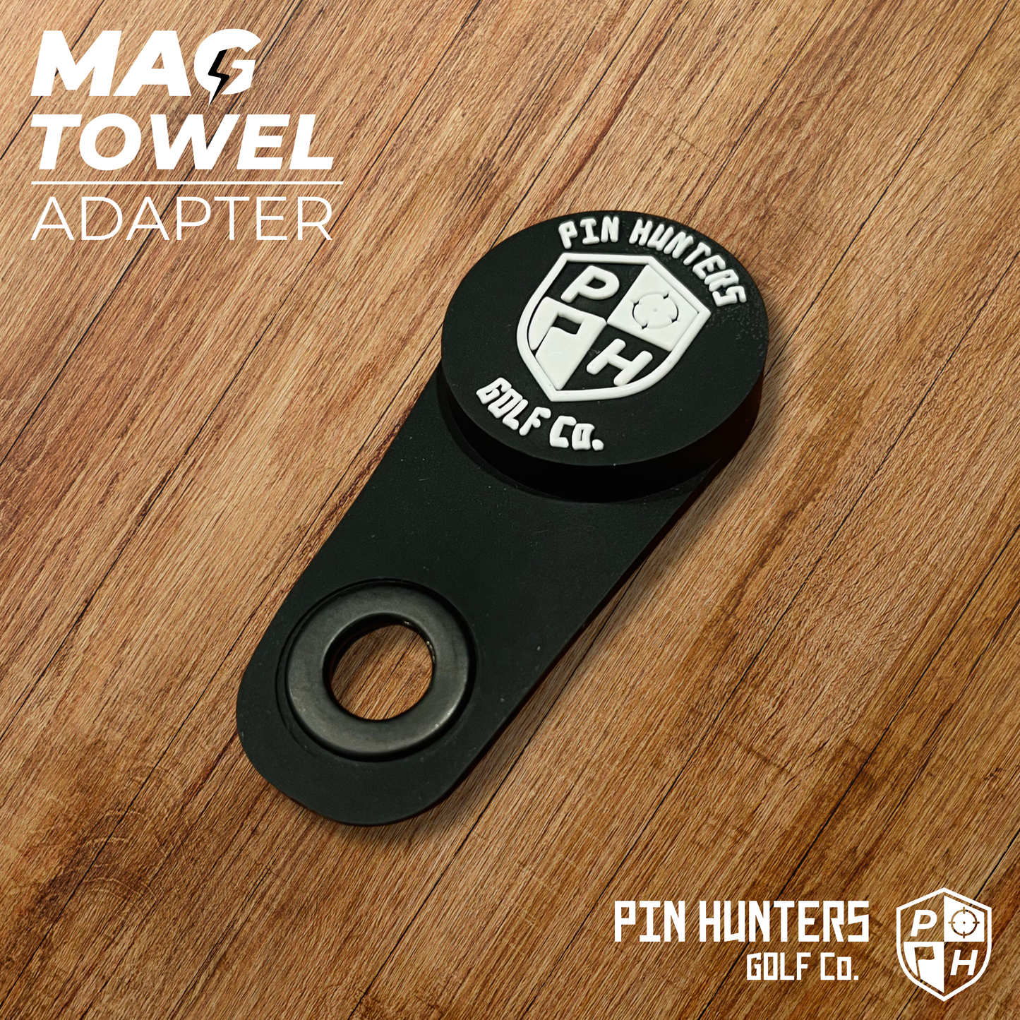 Pin Hunters Mag Towel Adapter shown on a wood surface with black magnetic attachment piece, carabiner hole, and Pin Hunters branding.