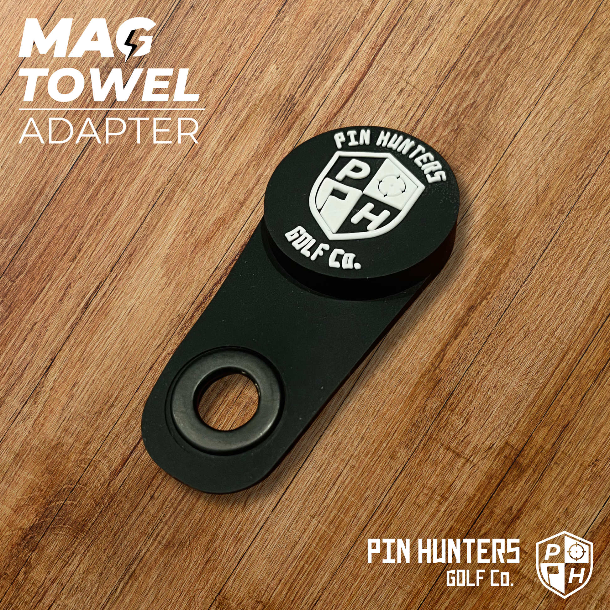 Pin Hunters Mag Towel Adapter shown on a wood surface with black magnetic attachment piece, carabiner hole, and Pin Hunters branding.