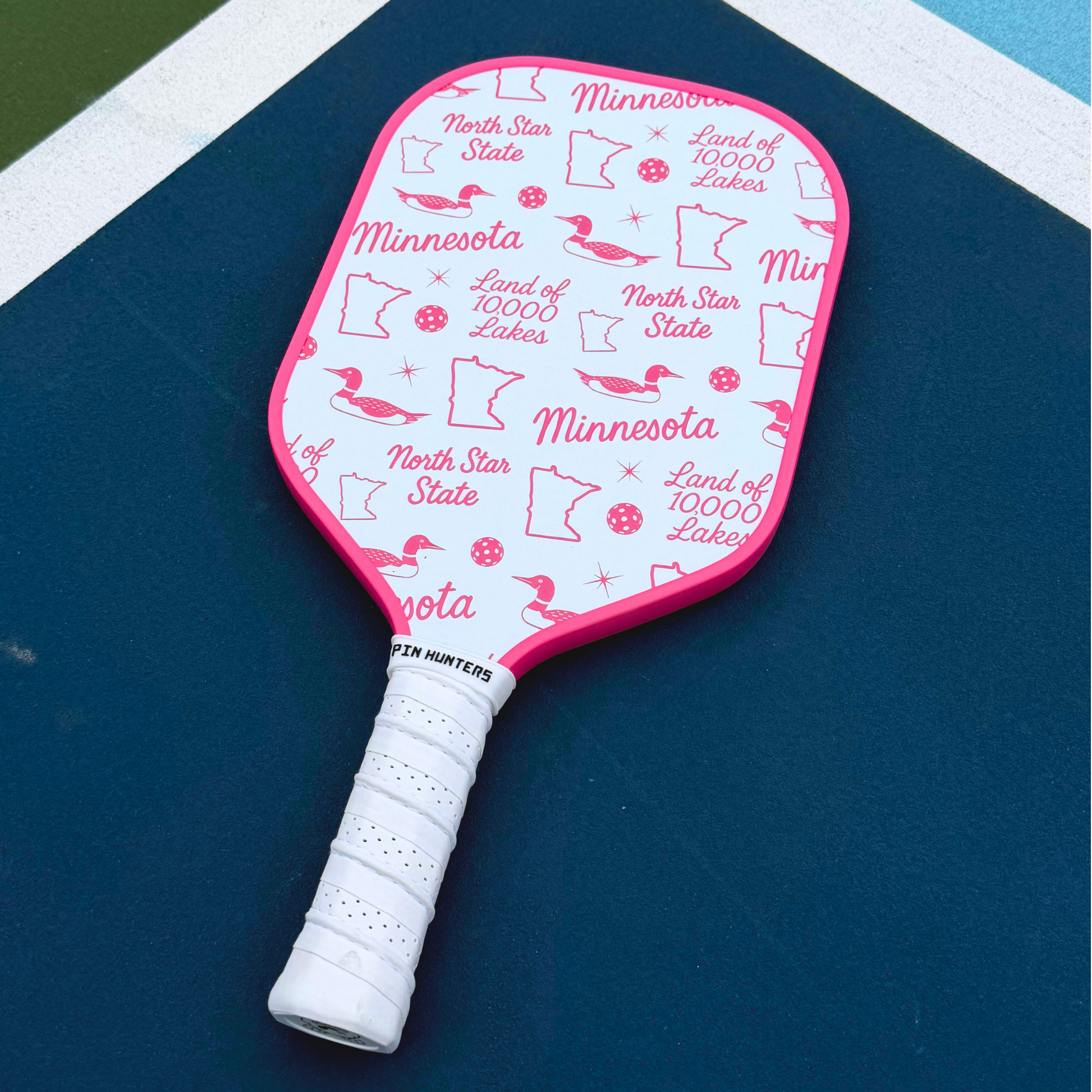 Pink Minnesota pickleball paddle with white handle, pink edge, loon icons, state outlines, and Land of 10,000 Lakes pattern.