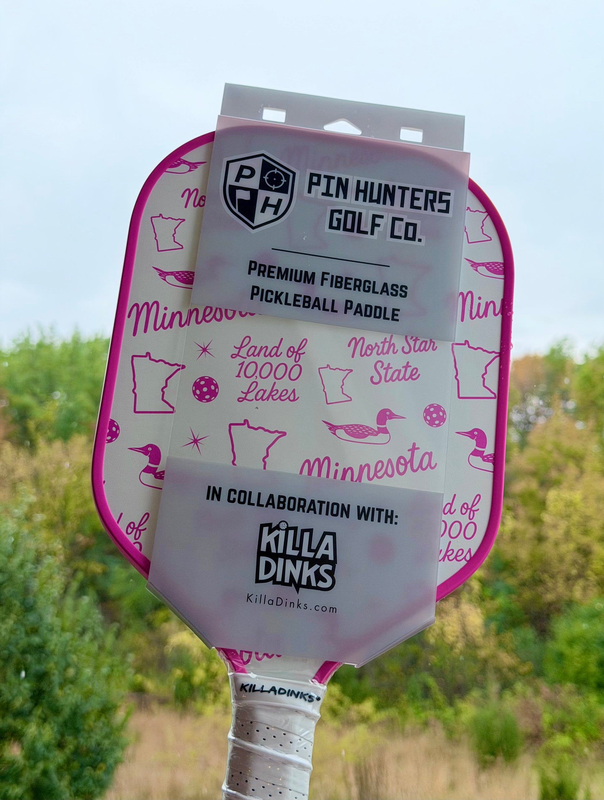 Pink Minnesota pickleball paddle in retail packaging with North Star State graphics, loons, Minnesota outlines, pink edge guard, and Killa Dinks collaboration label.