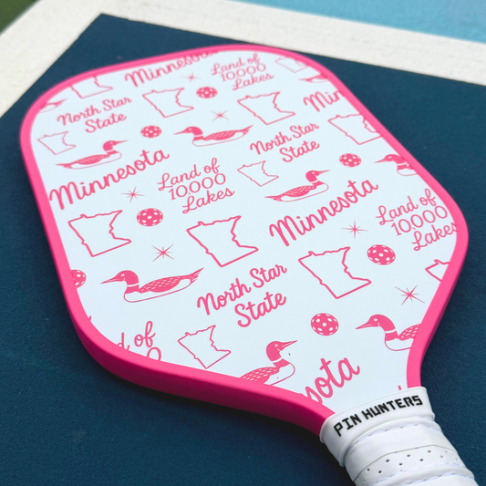 Close-up of a pink Minnesota themed pickleball paddle with loon, state outline, North Star State, and Land of 10,000 Lakes graphics.