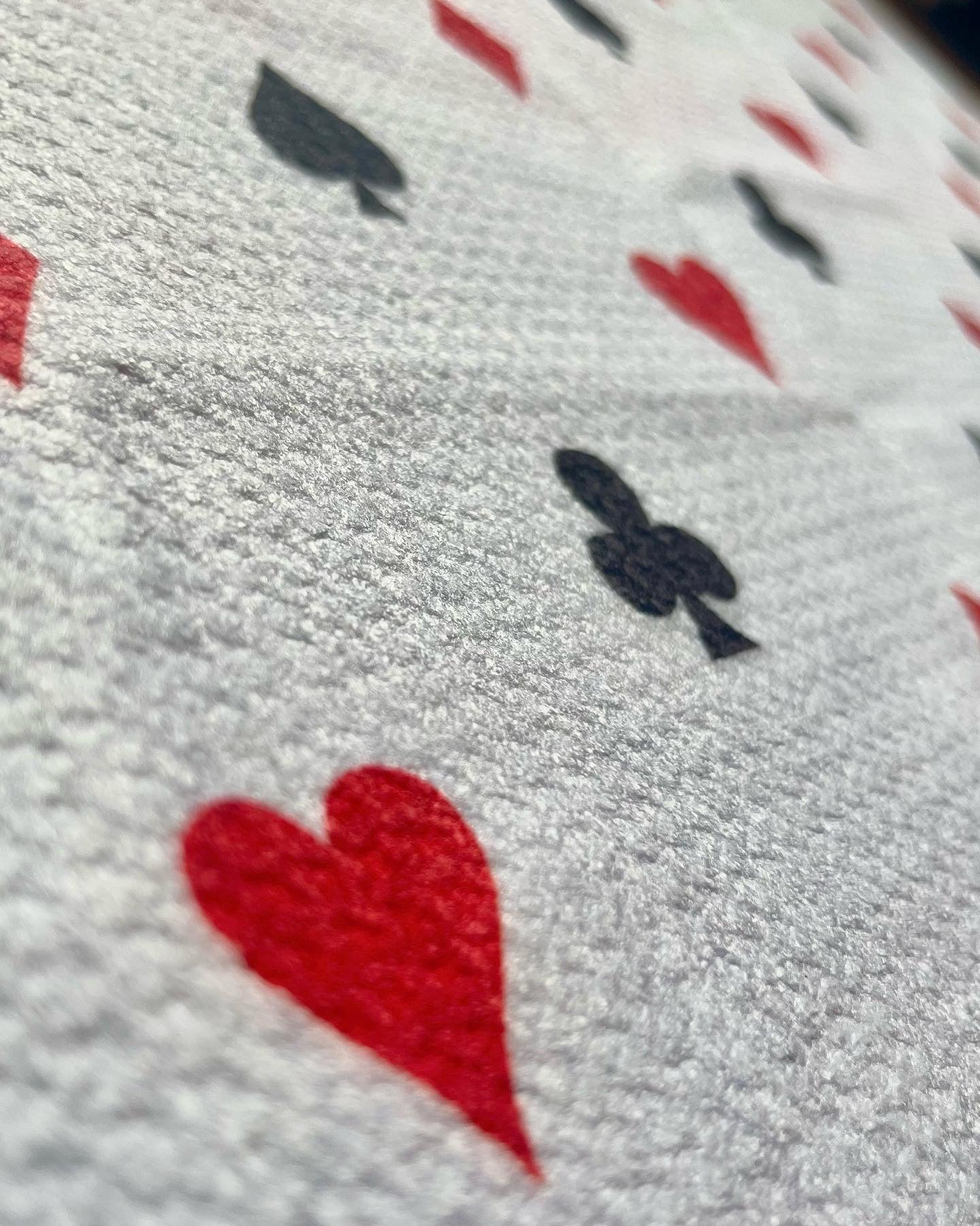Close up of a poker card suits golf towel with red hearts, black clubs, spades, and microfiber towel texture.