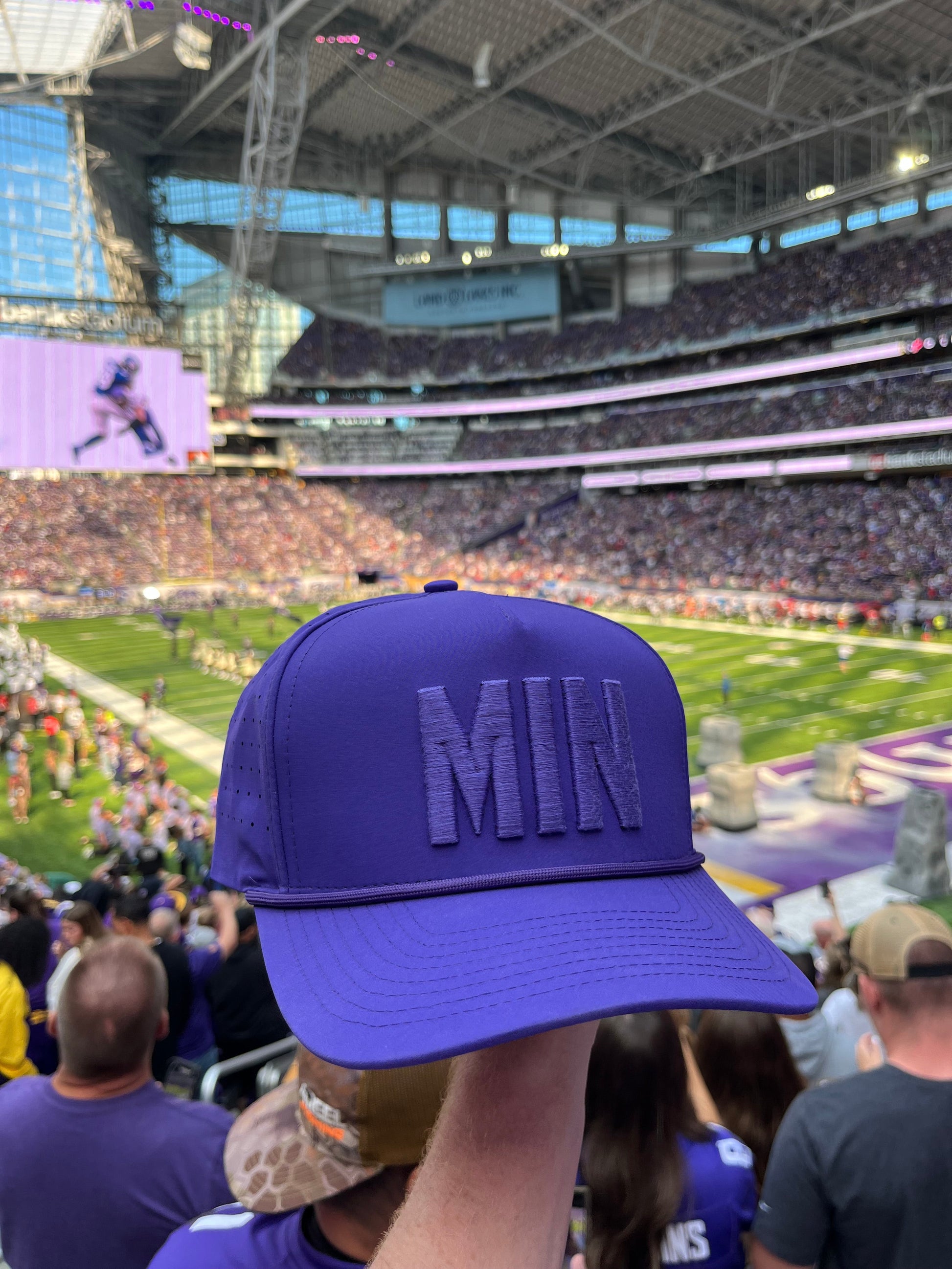 Close-up of the purple MIN Performance Hat by Pin Hunters Golf Co. showing tonal raised MIN embroidery and rope detail outdoors.