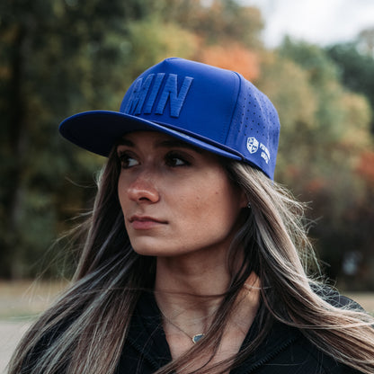 Woman wearing the purple Minnesota Vikings MIN Performance Hat by Pin Hunters Golf Co. outdoors, showing tonal raised MIN embroidery, rope detail, and perforated side panels.
