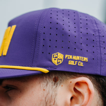 Close up of purple performance hat side panel with yellow Pin Hunters Golf Co. logo embroidery, perforated ventilation holes, and yellow rope trim.