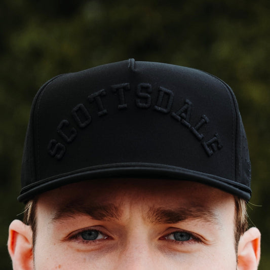 Blackout Scottsdale performance hat lifestyle view with tonal black raised embroidery, black rope, and curved front lettering.