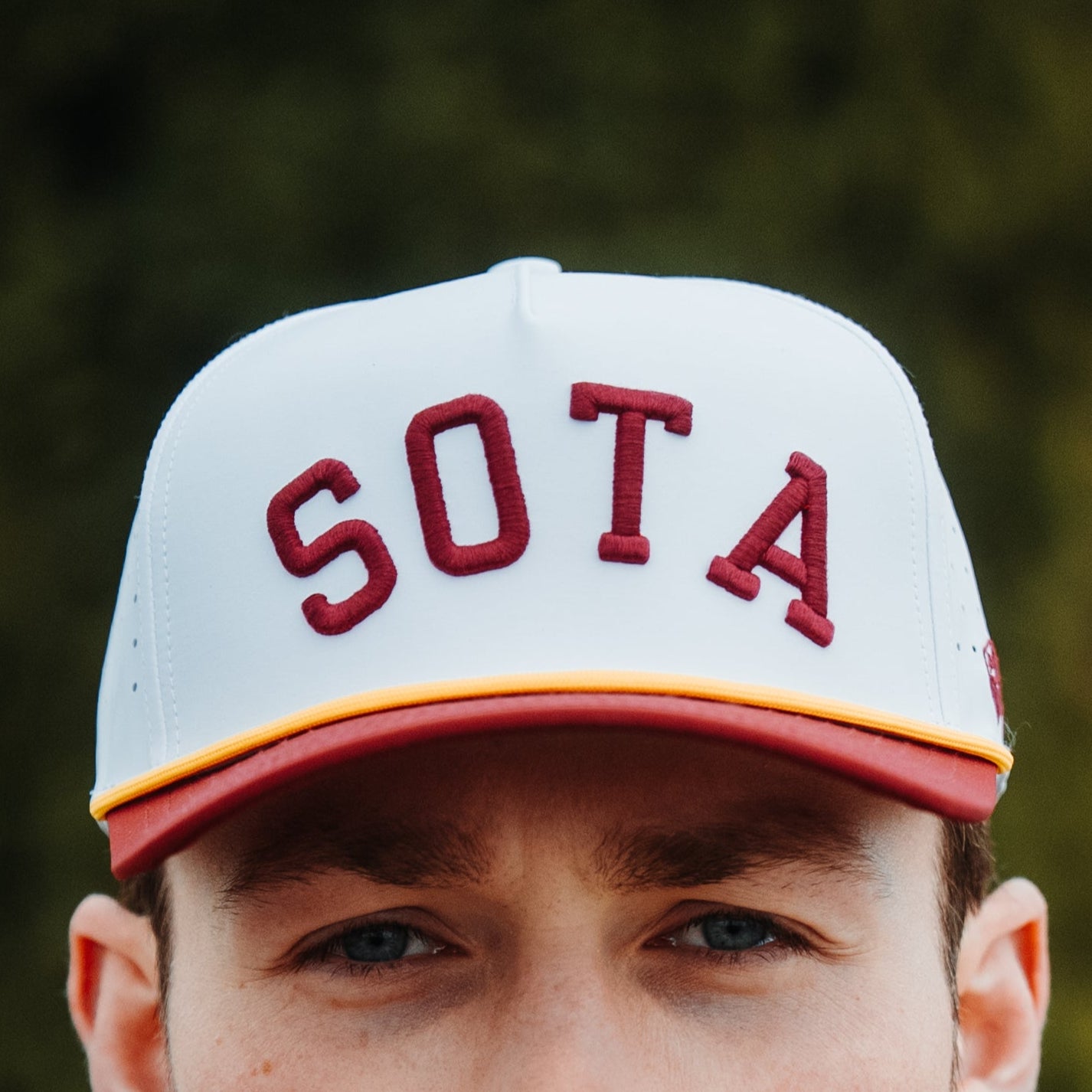 Front view of white and maroon SOTA performance hat with maroon raised SOTA embroidery, gold rope, and flat maroon brim.