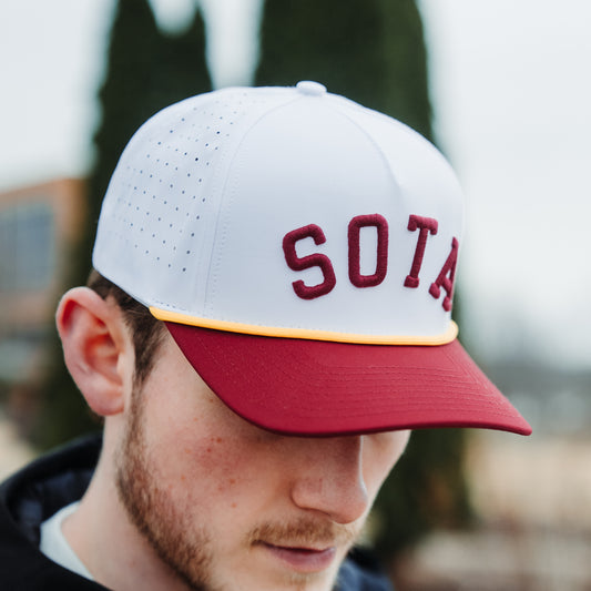 White and maroon SOTA performance hat worn outdoors with maroon raised embroidery, gold rope, maroon brim, and perforated side panels.