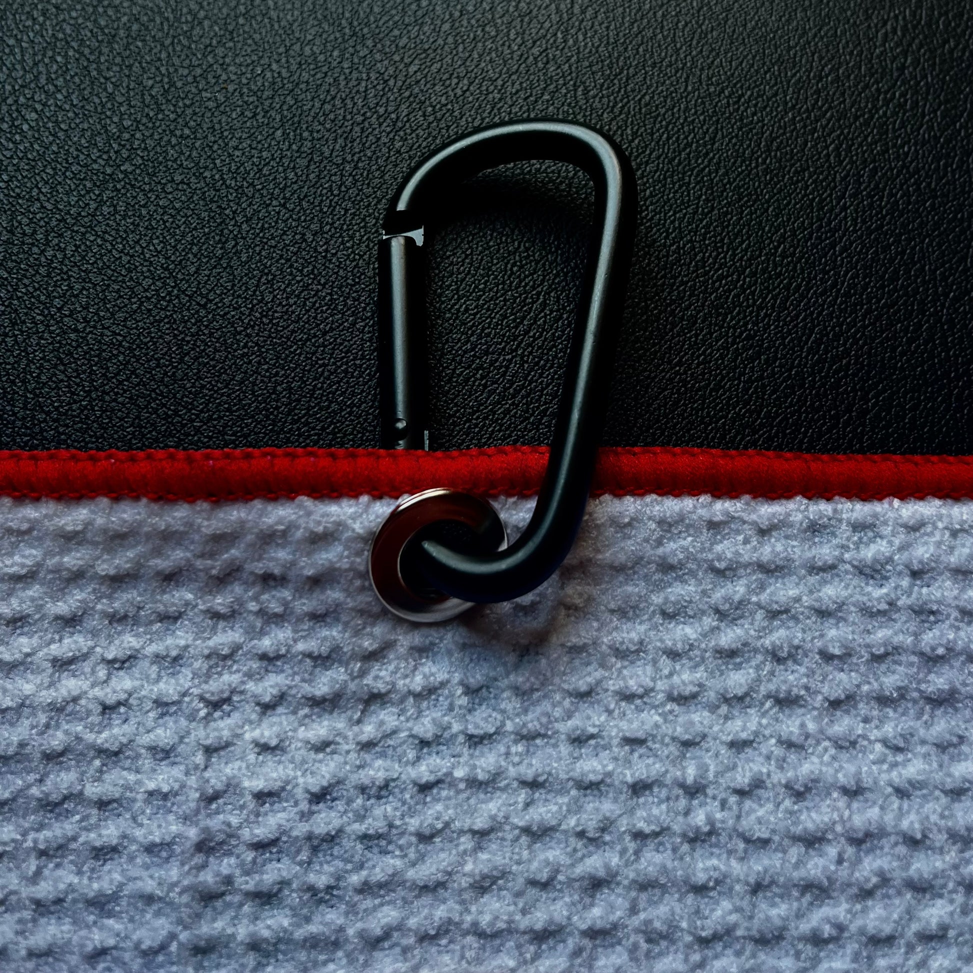 Close up of a black carabiner clipped to a Tennessee flag inspired golf towel with red trim and white microfiber fabric.
