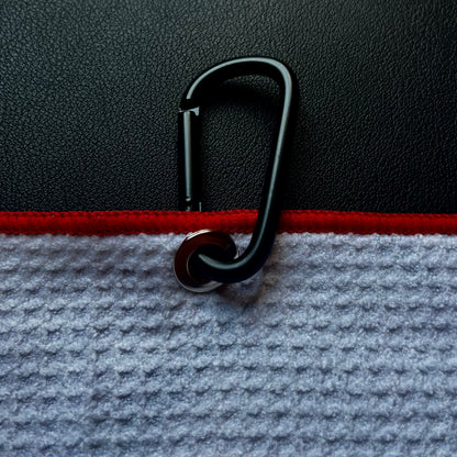 Close up of a black carabiner clipped to a Tennessee flag inspired golf towel with red trim and white microfiber fabric.