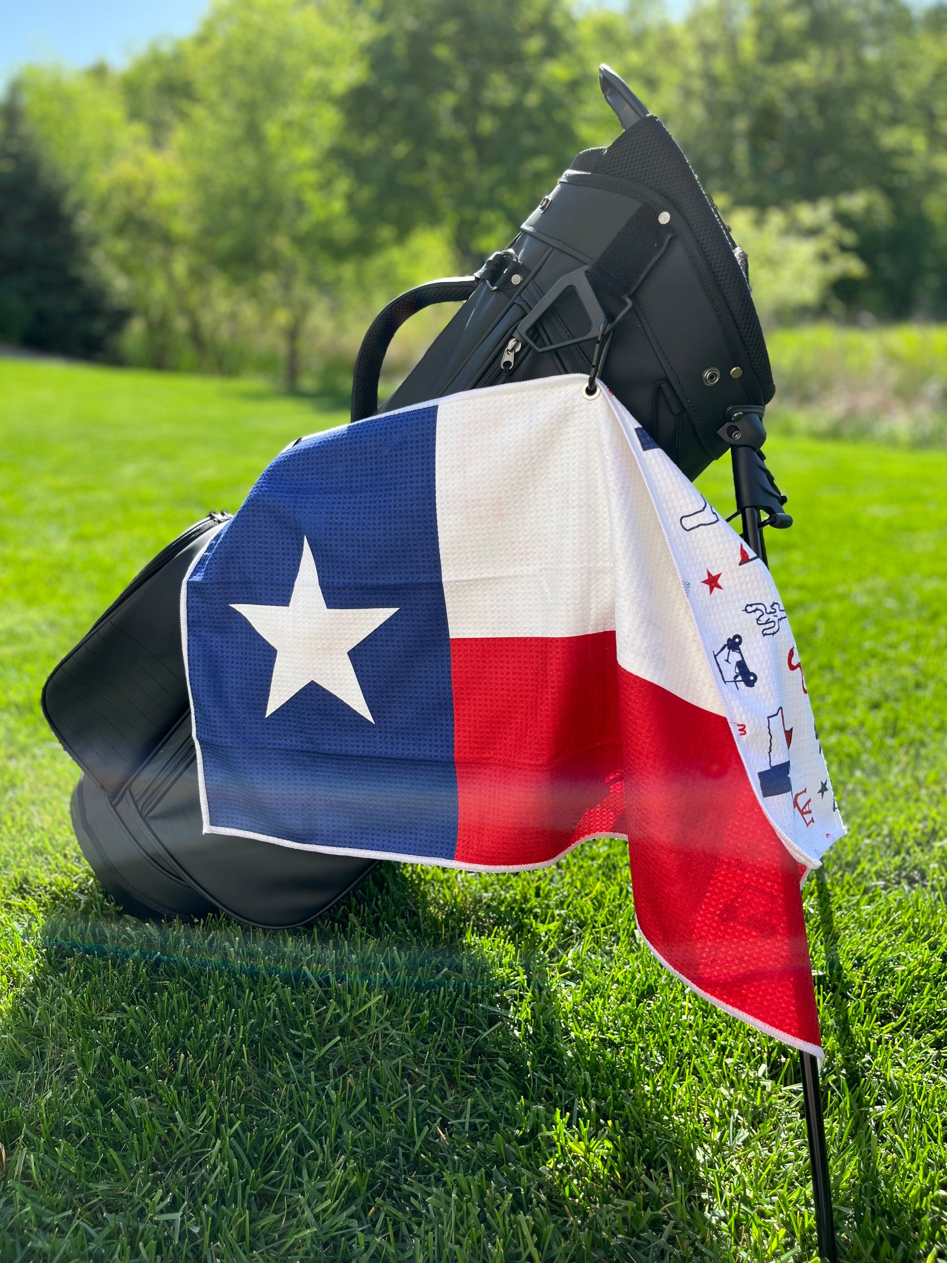 Texas flag golf towel hanging from a black golf bag with the large blue, white, and red Texas flag front design visible.