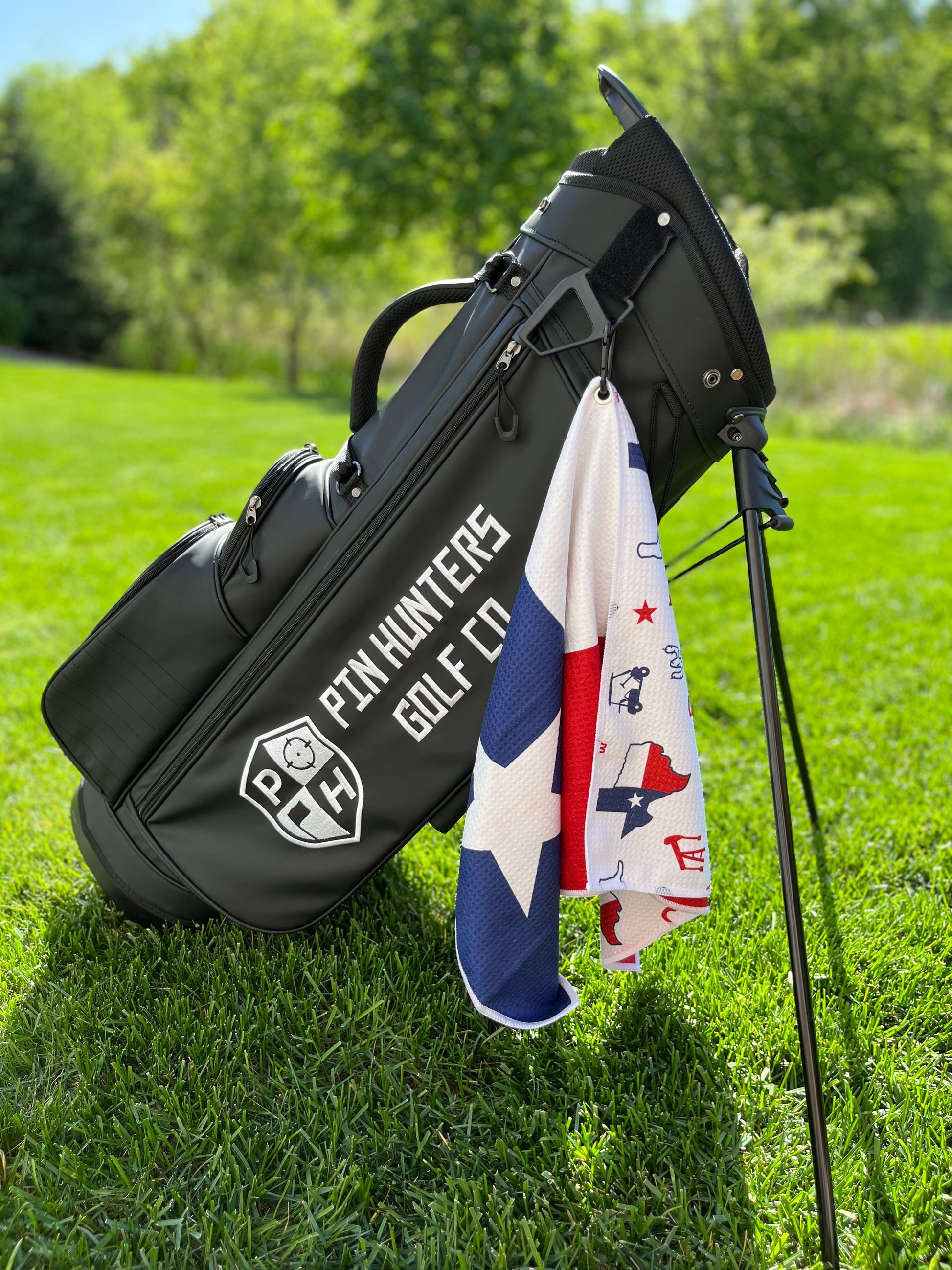 Texas flag golf towel hanging from a black Pin Hunters golf bag, showing the blue star front and red, white, and blue Texas themed back pattern.