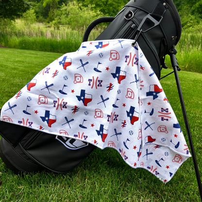 Texas Rangers white golf towel hanging on a black golf bag with TX baseball text, Texas flag state outlines, baseballs, baseball diamonds, golfers, and golf flags.