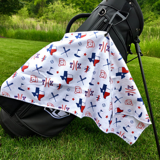 Texas Rangers white golf towel hanging on a black golf bag with TX baseball text, Texas flag state outlines, baseballs, baseball diamonds, golfers, and golf flags.