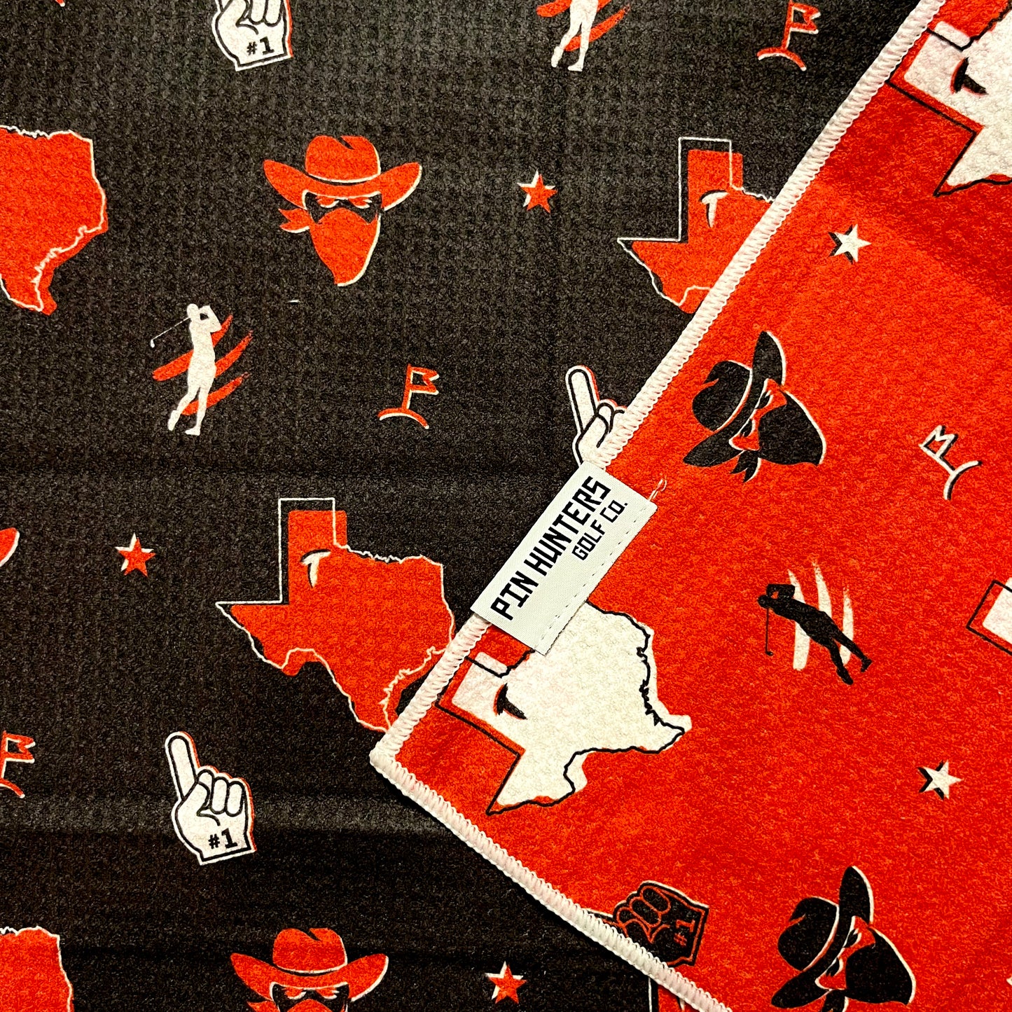 Close up of Texas Tech golf towel with black and red Texas, cowboy hat, foam finger, golfer, and golf flag graphics.