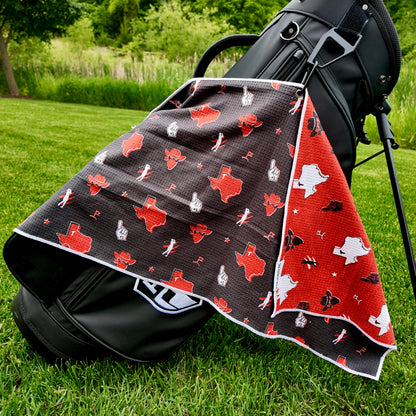 Texas Tech Red Raiders black golf towel hanging on a black golf bag with red Texas outlines, cowboy hats, foam fingers, golfers, golf flags, and red reverse side.