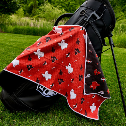Texas Tech Red Raiders red golf towel hanging on a black golf bag with white Texas outlines, black and red graphics, cowboy hats, foam fingers, golfers, and black reverse side.