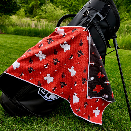 Texas Tech Red Raiders red golf towel hanging on a black golf bag with white Texas outlines, black and red graphics, cowboy hats, foam fingers, golfers, and black reverse side.