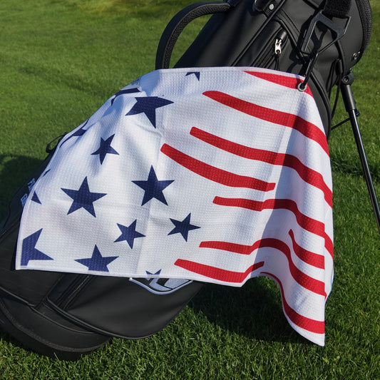 USA 1776 golf towel hanging on a black golf bag with navy stars, red stripes, white microfiber waffle fabric, and patriotic American flag design.