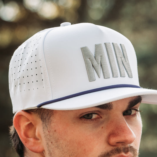 White MIN performance golf hat with gray raised embroidery, purple rope detail, perforated side panels, and model close-up.