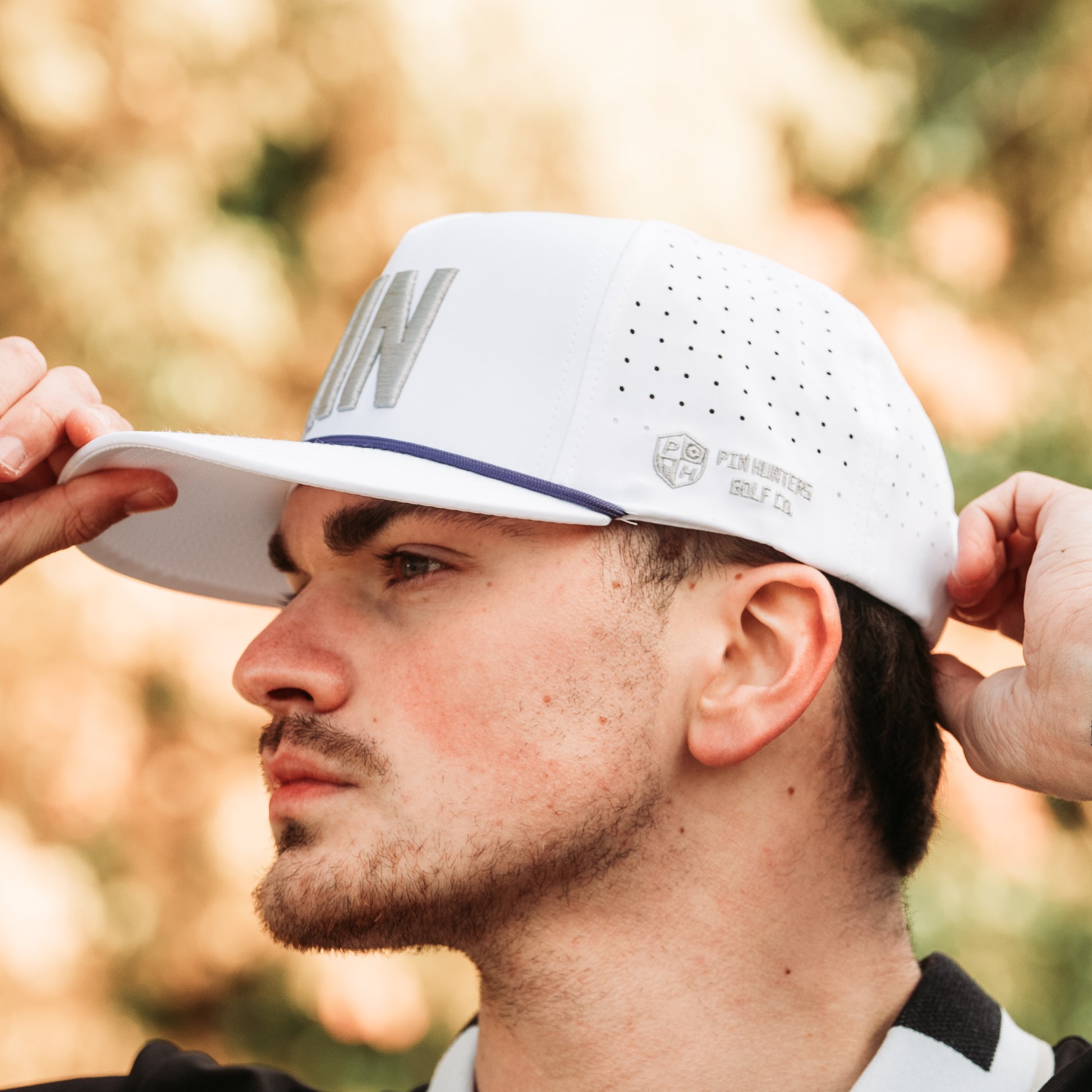 White MIN performance golf hat with gray embroidery, purple rope detail, side logo embroidery, and perforated side panels.
