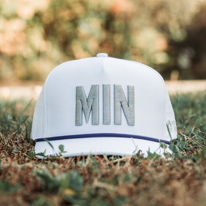White MIN vikings whiteout warrior performance golf hat on grass with gray raised MIN embroidery, purple rope detail, perforated side panels, and clean tonal design.