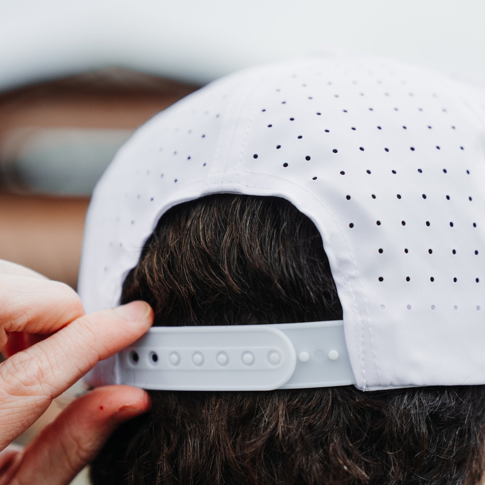 White performance golf hat back close-up with perforated panels, gray snapback closure, and model adjusting the strap.